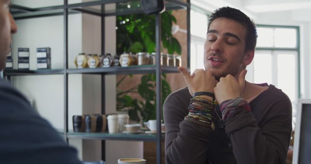 Young man having animated conversation with friend over coffee in a cozy café. Ideal for lifestyle, social interaction, casual meetings, and coffee culture themes.