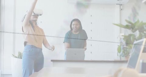 Young women collaborating with vr headset and laptop in modern open office workspace