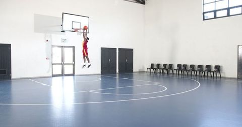 Athletic male dunking basketball in indoor gymnasium