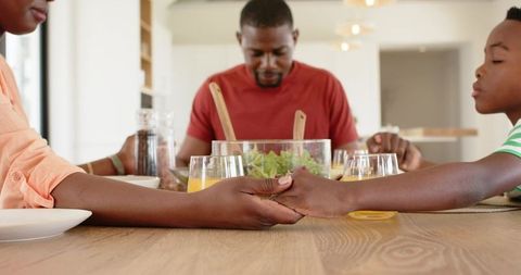 African american family holding hands at breakfast table sharing prayer and togetherness
