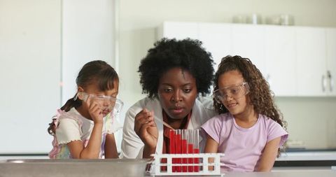 African female teacher guiding elementary students conducting colorful chemistry experiment