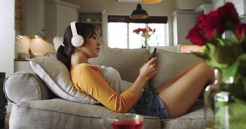 Woman Relaxing on Couch with Phone and Headphones in Cozy Home