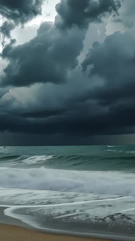 Gathering storm clouds stirring ocean swells and crashing white foam on sandy beach vertical video