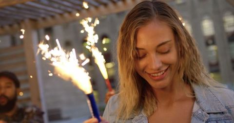 Joyful woman celebrating rooftop party with sparklers at dusk