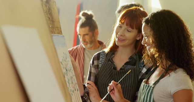 Women participating in an art class, painting on easels together, and sharing creative ideas. Useful for illustrating concepts of teamwork, creativity, art lessons, hobbies, and learning activities.