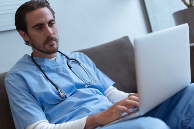 Front view of male surgeon using laptop on sofa in lobby at hospital