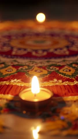 Vertical video sliding forward toward glowing tealight on colorful rangoli for festive ambiance
