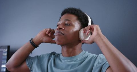 Young man adjusting wireless over-ear headphones while listening to music in home workspace