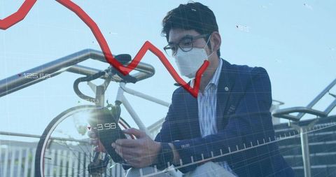Businessman wearing face mask checking smartphone with declining stock market graph overlay