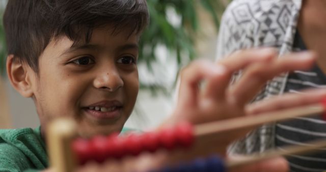 Young boy seen smiling while manipulating wooden abacus beads. Ideal for educational content, learning environments, child development articles, school promotional materials.