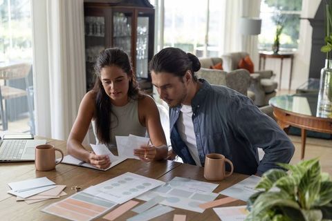 Young couple reviewing budget documents and color swatches at sunlit dining table