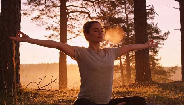 Woman meditating at sunrise in pine forest clearing, exhaling visible breath, mudra