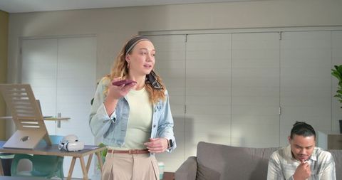 Woman speaking into smartphone while man using laptop in modern home workspace