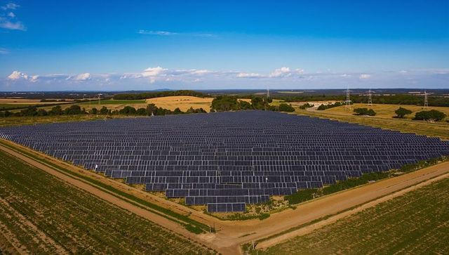 Aerial view of large ground-mounted solar farm on rural farmland with transmission lines