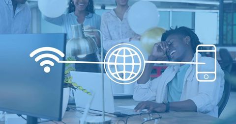 Laughing man leaning at desk in open-plan office celebrating team success with connectivity icons