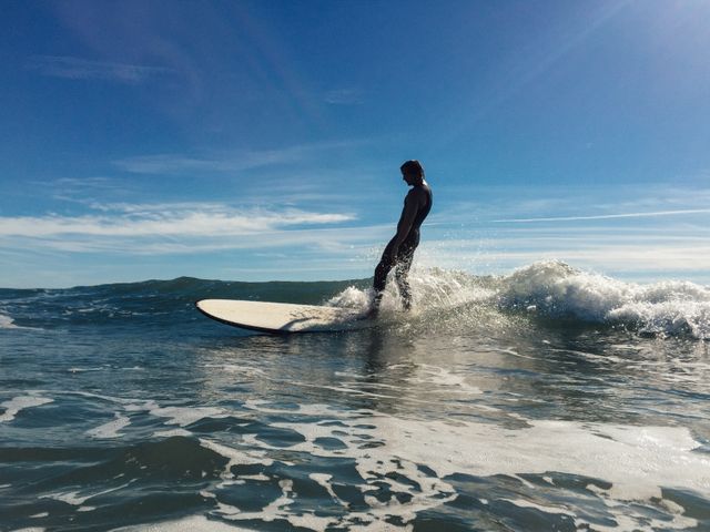 A surfer skillfully rides a wave under a clear, sunny sky. The dynamic movement of the water and the athleticism of the surfer make this perfect for promoting beach vacations, water sports equipment, travel blogs, and summer outdoor activities.