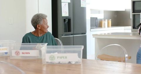 Senior african woman sorting recycling bins at kitchen table in modern home