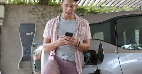 Man using smartphone while charging electric car at home station