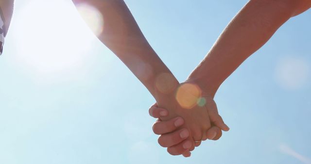 Two people are holding hands against a sunny sky, symbolizing connection and togetherness. The image captures a moment of affection or partnership, with the bright sun adding a warm, hopeful backdrop.