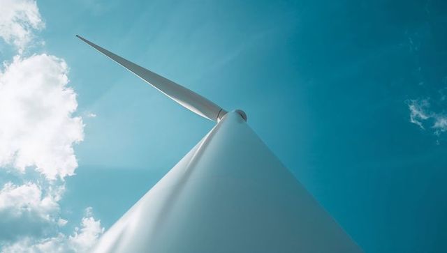 Wind Turbine Tower Rising Toward Blue Sky with Blade Tip and Minimalist Composition