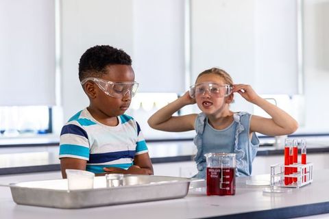 Black boy and white girl conducting science experiment in school lab wearing goggles