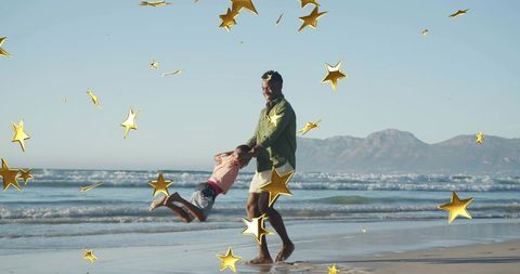 Father swinging son on sunlit beach with waves and distant mountains, gold star confetti