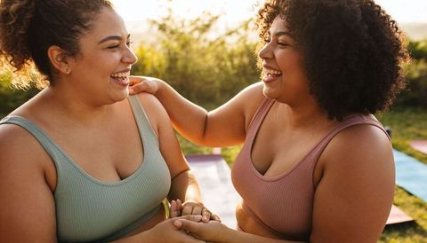 Two women laughing and holding hands on yoga mats outdoor wellness friendship backlit