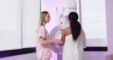 Mammography technician guiding patient into mammogram machine for breast cancer screening