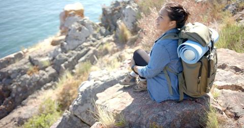 Woman Hiking in Mountains Resting with Backpack on Rocky Cliff