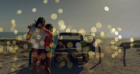 Couple walking toward pickup truck with surfboard at sunset on sandy beach