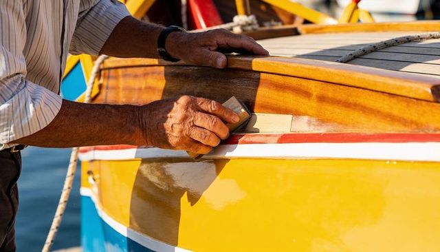 Sunlit hands sanding boat trim on marina dock restoring wooden craftsmanship with sandpaper
