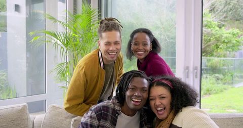 Laughing diverse friends leaning forward on cozy sofa sharing bright modern living room