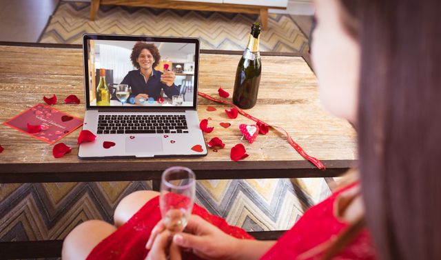 Biracial young man showing ring to biracial girlfriend having champagne during online dating. unaltered, online dating, video call and distant valentine day celebration.
