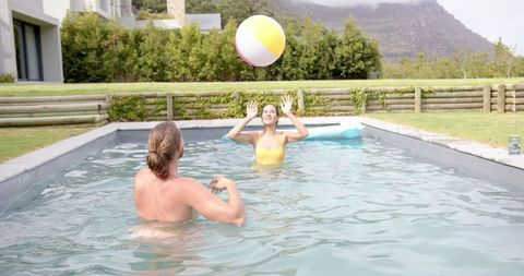Joyful couple playing with beach ball in backyard pool
