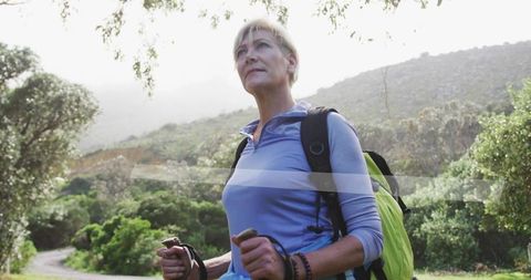 Senior Woman Hiking with Trekking Poles Among Green Hills