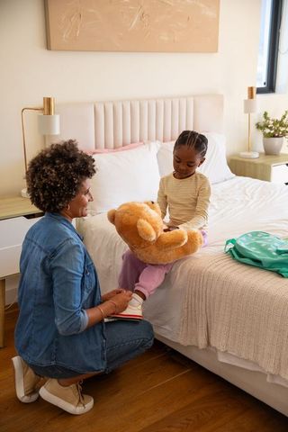 Loving Mother Tying Daughter's Shoelaces in Cozy Bedroom