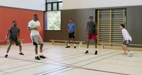 Multicultural young men playing indoor basketball, dribbling and passing in teamwork drill