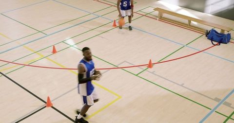 African american players dribbling agility drill on indoor basketball court with cones