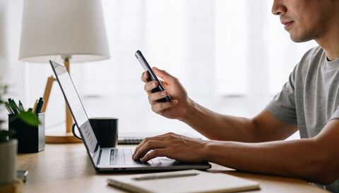 Adult man multitasking on laptop and smartphone at tidy home desk remote work productivity