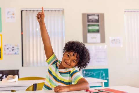 African american boy raising hand in classroom smiling, participating in elementary lesson