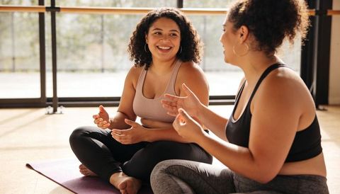 Two Women Laughing and Chatting After Yoga Class on Sunlit Studio Mats for Wellness