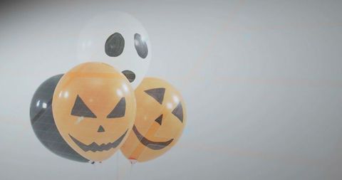 Floating halloween balloons showing jack-o'-lantern and ghost faces on neutral background