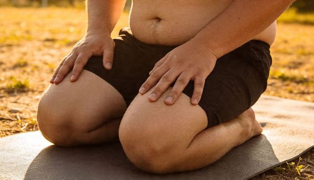 Kneeling shirtless man resting hands on thighs on yoga mat in sunlit dry grass fitness pose