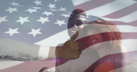 Black couple giving thumbs-up on sunny beach with american flag overlay