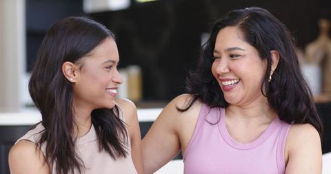 Two women laughing and smiling on sofa in modern kitchen sharing warm friendship moment