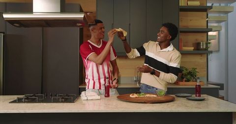 Diverse male friends enjoying pizza together in modern kitchen