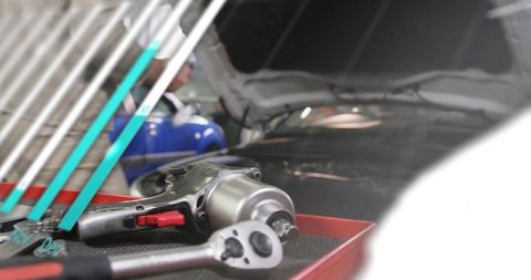 Mechanic repairing car using impact wrench on red tray near hood open vehicle in garage