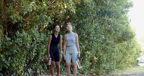 Female friends walking in park with water bottles engaging in conversation