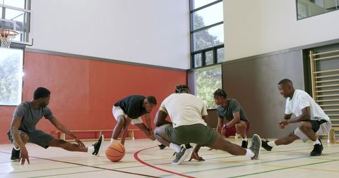 Team warm-up drills: five players performing side lunges and ball work on indoor court