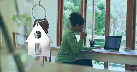 Working from home with house keychain concept: woman sipping coffee and checking laptop